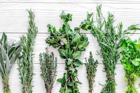 Fresh herbs and greenery for spices and cooking on white wooden kitchen desk background top viewの写真素材