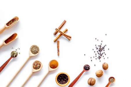 Variety of spices and dry herbs in wooden spoons on white kitchen table background top view mock-upの写真素材