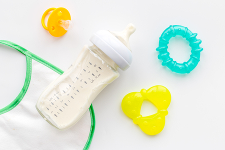 bottle with breastmilk and infant formula powdered healthy food, toys and bib on white desk...