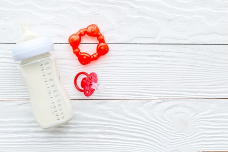 bottle with breastmilk and infant formula powdered healthy food, toys on white wooden desk...