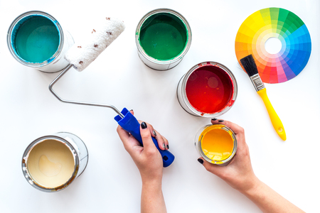 Choosing color for painting. Hands hold brush and paint roller on white background top view.の写真素材