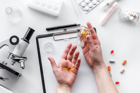 Do medcal tests. Hands hold pills near microscope on white background top view.の写真素材