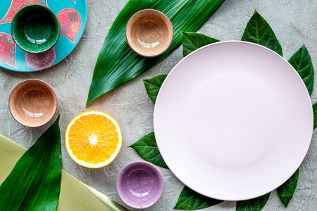 Empty plate mockup. Cups and plates near tropical leaves and fruits on grey background top view.の写真素材