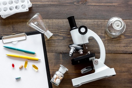 Laboratory test. Microscope, pills, test tube on wooden background top view.