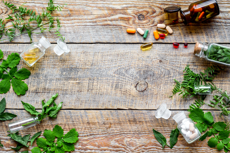 Healing herbs. Fresh leaves, bottles and pills on wooden background top view.の写真素材