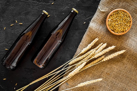 Preparing beer. Barley near beer bottle and glass on black background top view.