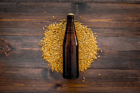 Grains of malting barley near beer bottle on wooden background top view.の写真素材