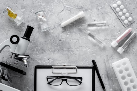 Doctor's workplace. Microscope, pills and test tube on grey stone background top view.