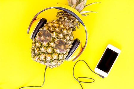 Stylish pineapple in sunglasses listen to music on the smartphone on yellow background top view.の写真素材