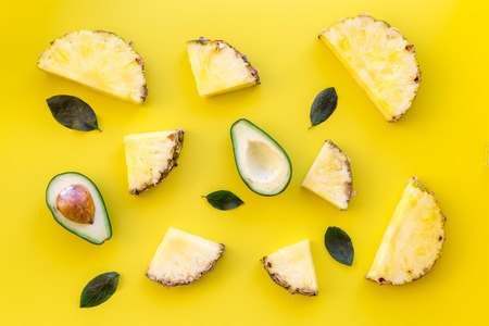 Exotic fruits pattern. Pinneapple and avocado slices on yellow background top view.の写真素材