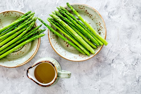 Cooking fresh asparagus. Greens on plate near a jug of oil on grey stone background top view.の写真素材
