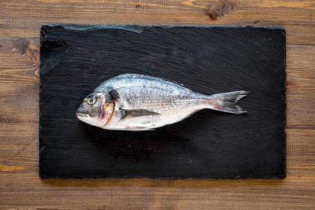 Fresh dorado fish ready to cook on black desk on wooden background top view.の写真素材