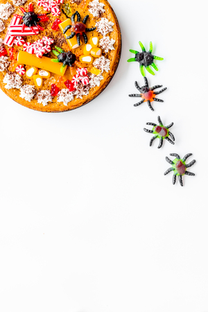Gummy spiders crawls toward pie for halloween on white background top view.の写真素材