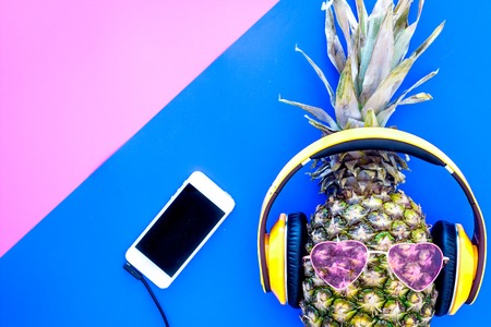 Stylish pineapple in sunglasses listen to music on the smartphone on blue and pink background top view copyspaceの写真素材