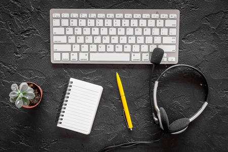 Workspace at call center. Headphones and notebook near keyboard on black background top view