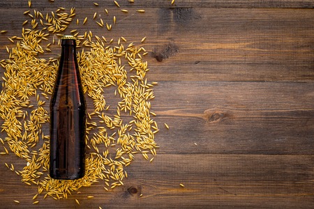 Grains of malting barley near beer bottle on wooden background top view.の写真素材