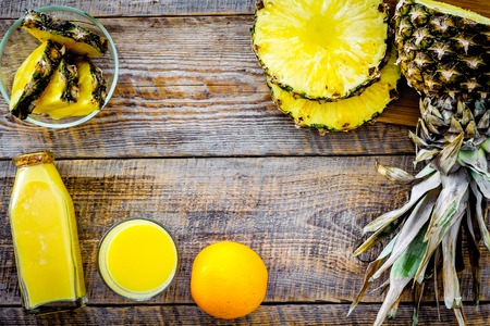 Tropical fruits juice. Bottle with beverage near pineapples slices on wooden background top view.の写真素材