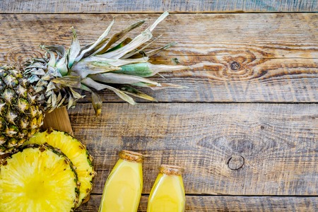 Tropical fruits juice. Bottle with beverage near pineapples slices on wooden background top view.の写真素材