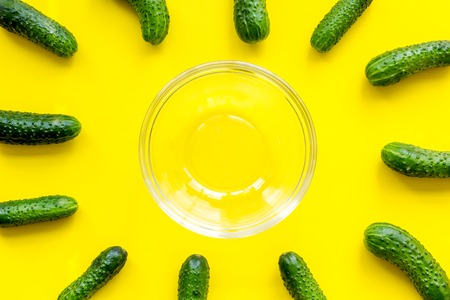 Make salad with fresh cucumbers. Vegetables near empty bowl on yellow background top view.の写真素材