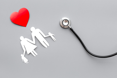 Take out health insurance for family. Stethoscope, paper heart and silhouette of family on grey background top viewの写真素材
