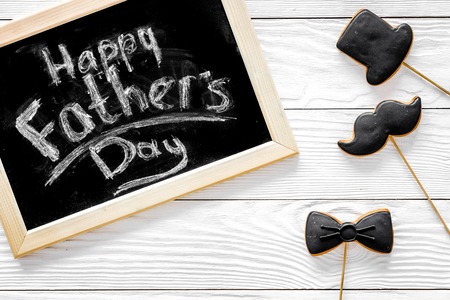 Words happy Fathers day written on blackboard. Black tie, mustache and hat cookies. White wooden background top viewの写真素材