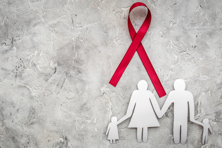 Red ribbon for HIV, AIDS, substance-abuse and anorexia awareness near paper silhouette of family on grey stone background top view.の写真素材