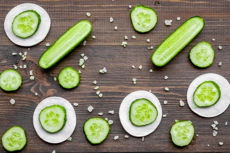 Skin care at home. Sliced cucumber pattern on dark wooden background top view.の写真素材