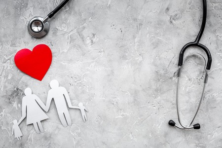 Take out health insurance for family. Stethoscope, paper heart and silhouette of family on grey background top view.の写真素材