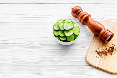Slices of fresh cucumbers in the bowl near paperbox. White wooden background copyspaceの写真素材