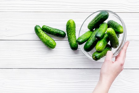 Hand takes bowl with fresh cucumbers. Grey wooden background top view copyspaceの写真素材