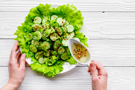 Hands season the salad with fresh cucumbers and lettuce with olive oil. Grey wooden background top view.の写真素材