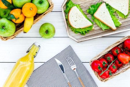 Healthy food for picnic. Sanwiches, fruits, vegetables, juice on tablecloth on white wooden background top viewの写真素材
