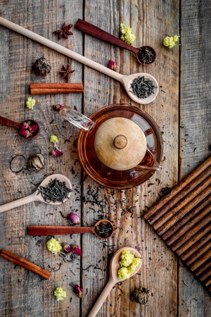 Brew tea with flowers and spices. Dried leaves and petals near tea pot on wooden background top viewの写真素材