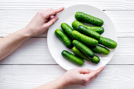 Hand takes plate with fresh cucumbers. Grey wooden background top viewの写真素材