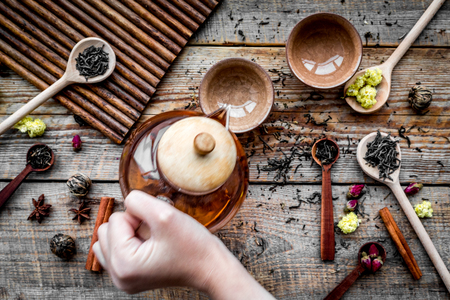Brew tea with flowers and spices. Pour the tea. Hand hold tea pot on wooden background top viewの写真素材