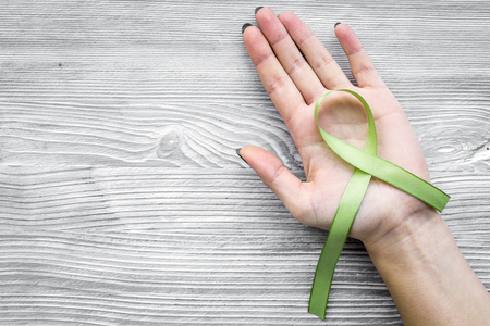 Hand hold green ribbon for Lyme disease, kidney cancer, organ donation awareness on grey wooden background top view copyspaceの写真素材