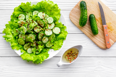 Salad with fresh cucumbers and lettuce near gravy boat. Grey wooden background top viewの写真素材