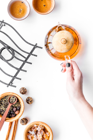 Tea ceremony concept. Hand takes tea pot near cups and dry tea leaves on white background top view copyspaceの写真素材