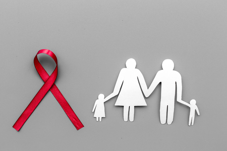 Red ribbon for HIV, AIDS, substance-abuse and anorexia awareness near paper silhouette of family on...