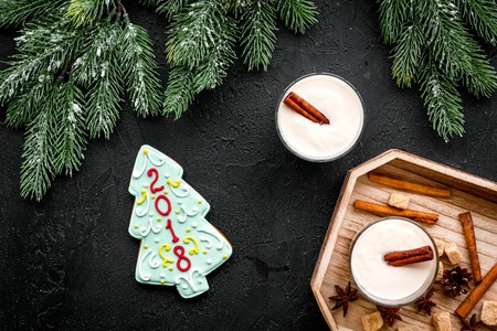 Homemade classic eggnog with cinamon and badian near spruce branch, pinecones, gingerbread on black background top viewの写真素材
