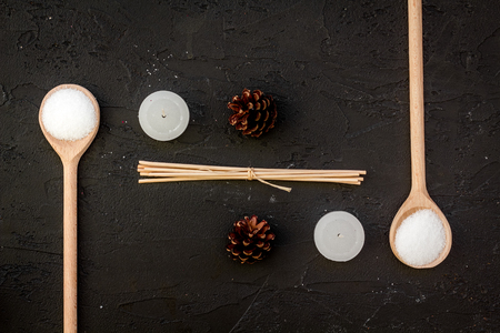 Skin care and relax. Cosmetics and aromatherapy concept. Pine spa salt and pinecones on black background top viewの写真素材