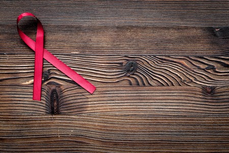 Red ribbon for HIV, AIDS, substance-abuse and anorexia awareness on dark wooden background top view copyspaceの写真素材
