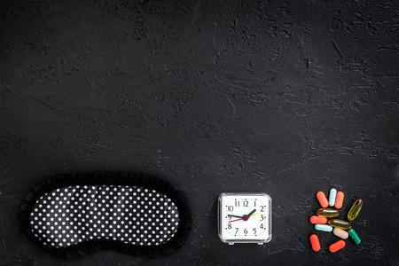 Combat insomnia. Sleeping pills near sleep mask and alarm clock on black background top view.の写真素材