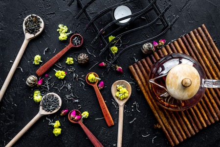 Brew the aromatic tea. Tea pot near wooden spoons with dried tea leaves, flowers and spices on black wooden background top viewの写真素材