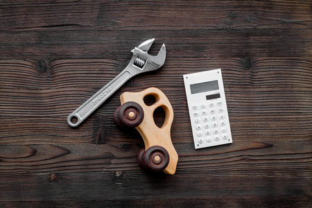 Price of car repair. Wrench near car toys and calculator on dark wooden background top viewの写真素材