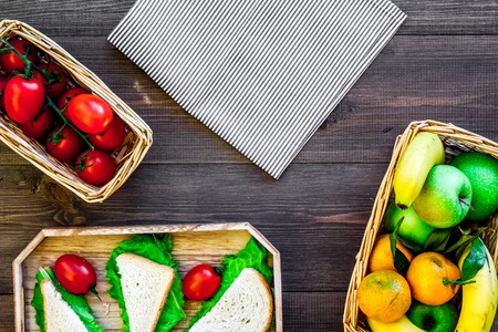 What bring for a picnic. Sanwiches, fruits, vegetables on tablecloth on dark wooden background top view copyspaceの写真素材