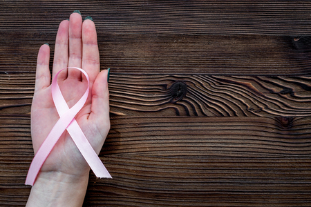 Hand hold pink ribbon for breast cancer awareness on dark wooden background top view copyspaceの写真素材