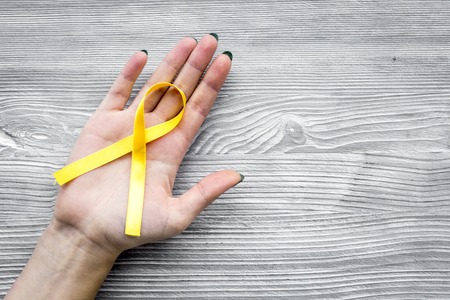 Woman hand hold yellow ribbon for suicide and endometriosis awareness on grey wooden background top view copyspaceの写真素材