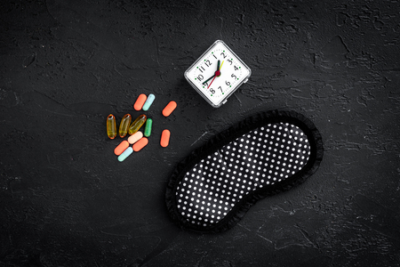 Combat insomnia. Sleeping pills near sleep mask and alarm clock on black background top viewの写真素材