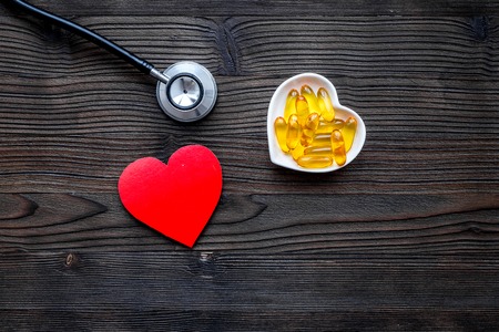 Treat heart. Pills in bowl in shape of heart on dark wooden background top view.の写真素材